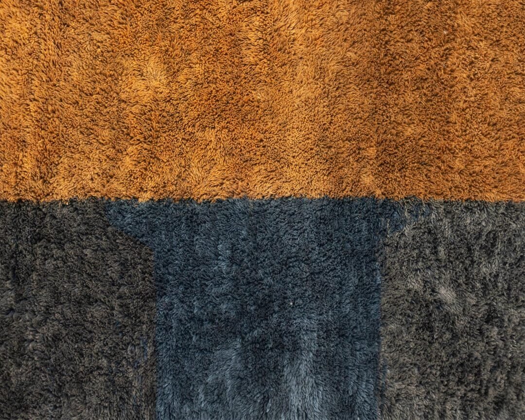 This close-up captures a vibrant rug featuring two distinct horizontal color blocks: the upper section showcases a warm orange-brown, while the lower section offers an expansive dark blue-gray.