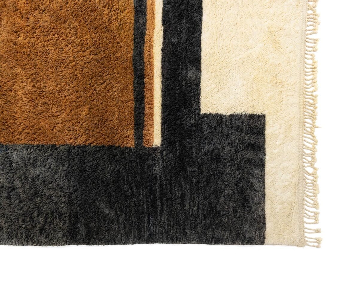 Close-up of a rug corner showcasing an abstract rectangular design in brown, black, and cream hues. Fringed edges appear on the right, adding tactile interest.