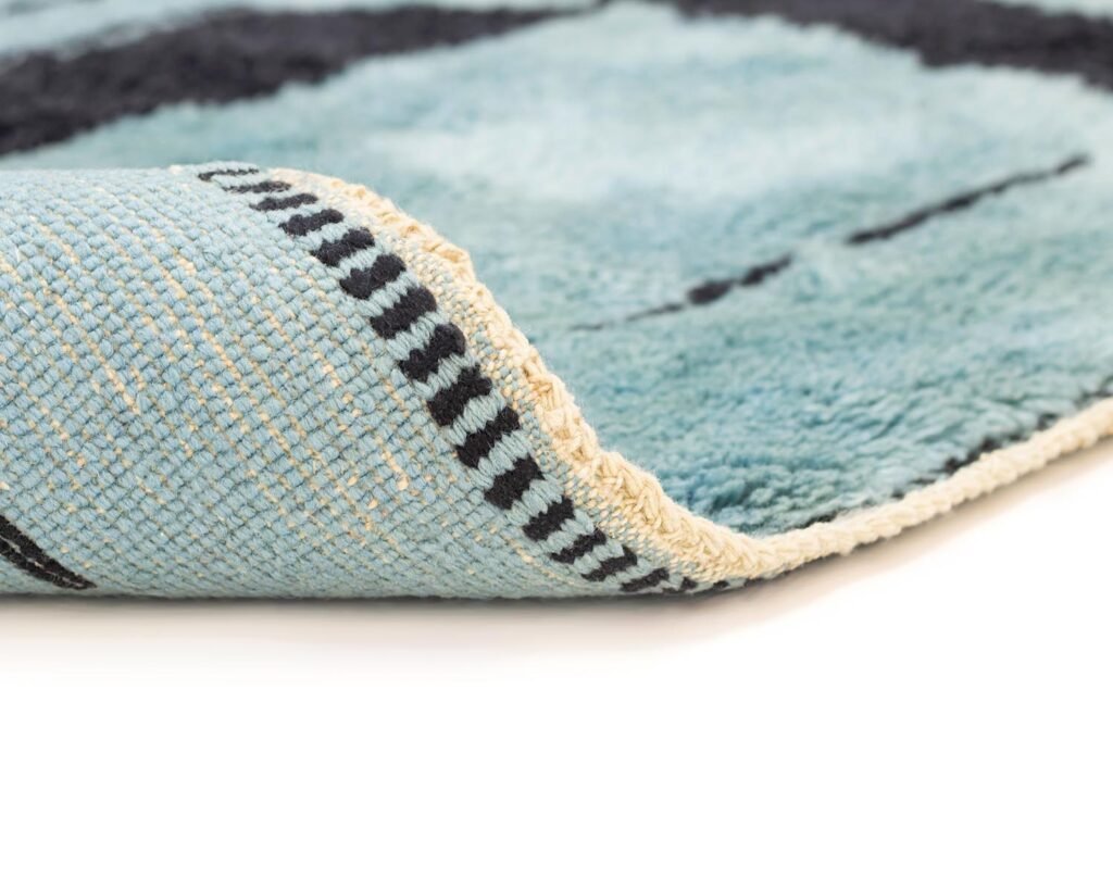 Close-up of a blue and beige rug corner with a geometric design, showing its texture and thickness.