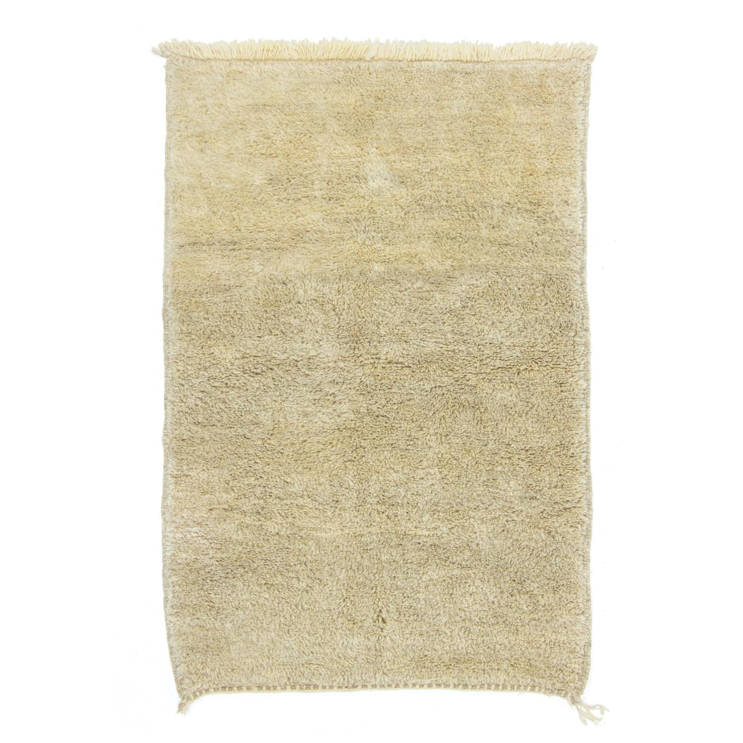 This authentic Moroccan rug features a rectangular shape with a shaggy texture and fringed edges on the shorter sides, showcasing its hand-knotted craftsmanship in a plain beige design.