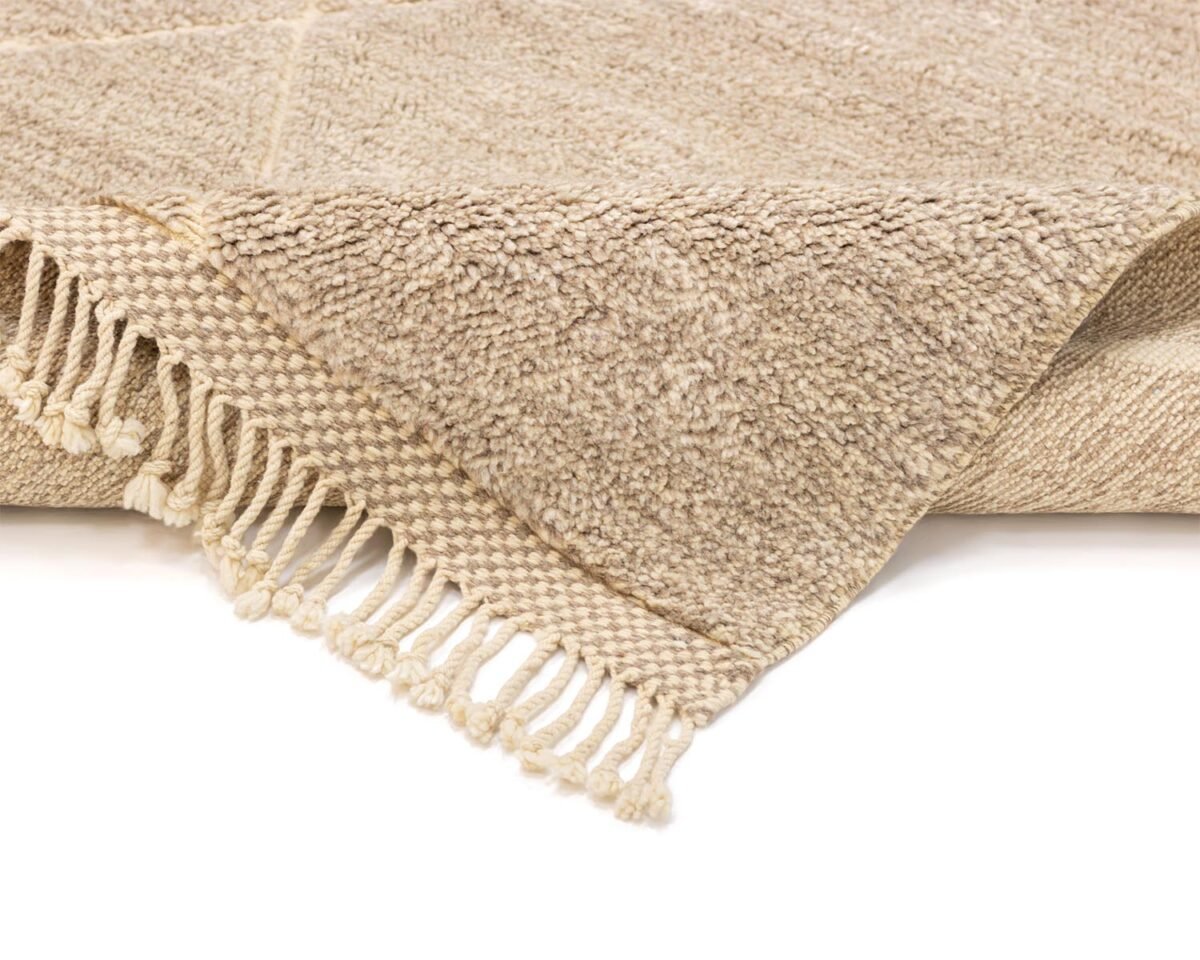 A close-up of a beige Moroccan rug with fringed edges, showcasing its intricate weave and soft pile.