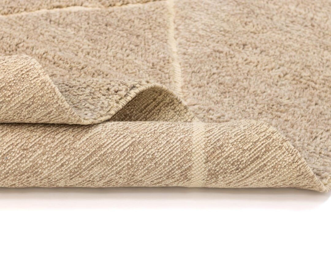 A close-up of a folded beige Moroccan rug with a textured surface, showcasing its thickness and intricately woven underside.