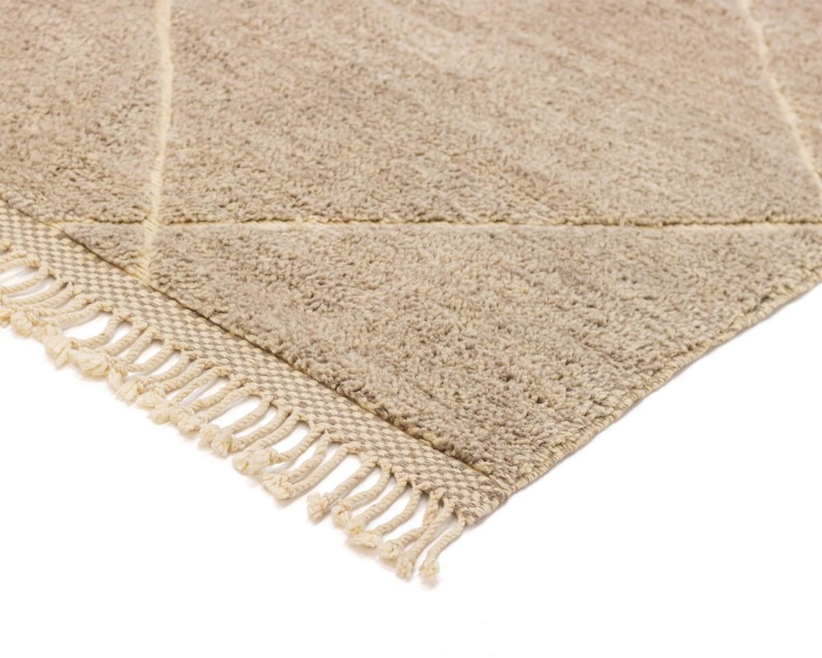 Close-up of a beige Moroccan rug corner with fringed edges, showcasing its textured surface and geometric pattern.