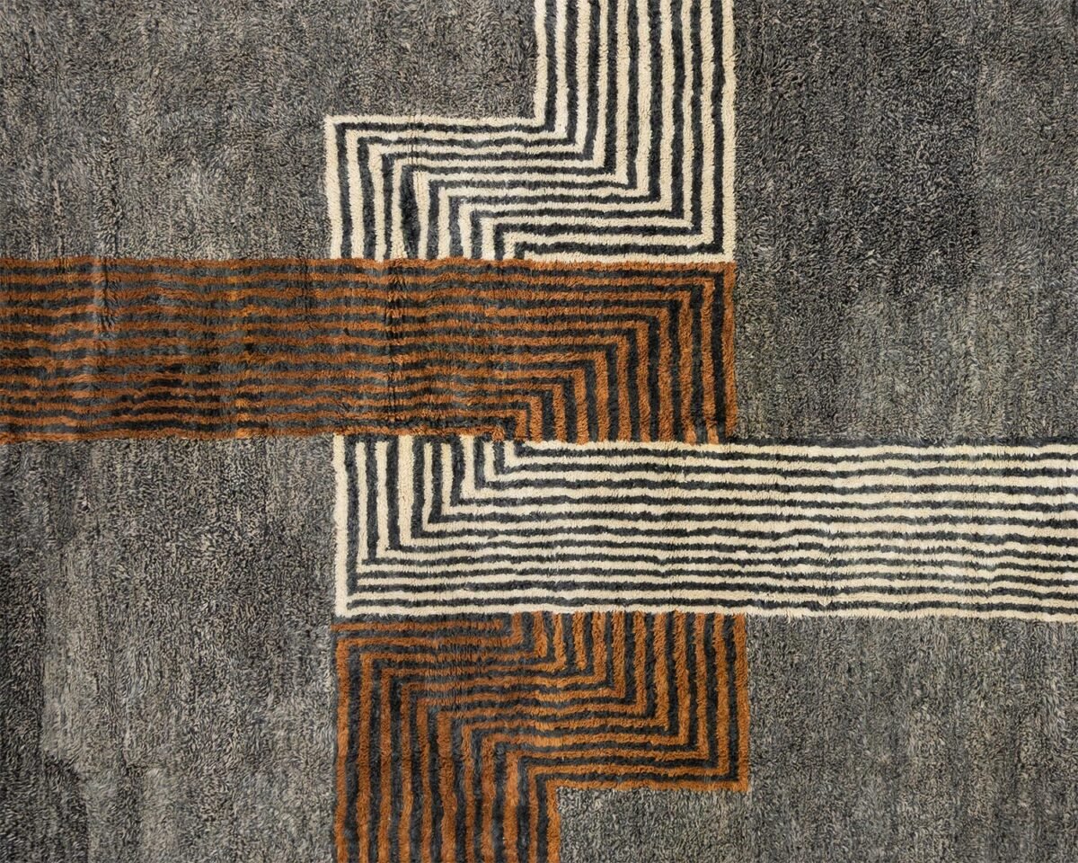 An abstract design with intersecting lines and rectangles in brown, white, and gray tones graces the surface of this artisanal rug.