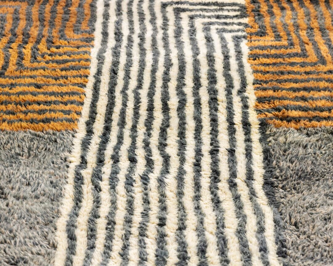 This close-up showcases an artisanal, hand-knotted rug featuring intricate patterns of white, black, orange, and gray stripes and zigzags.