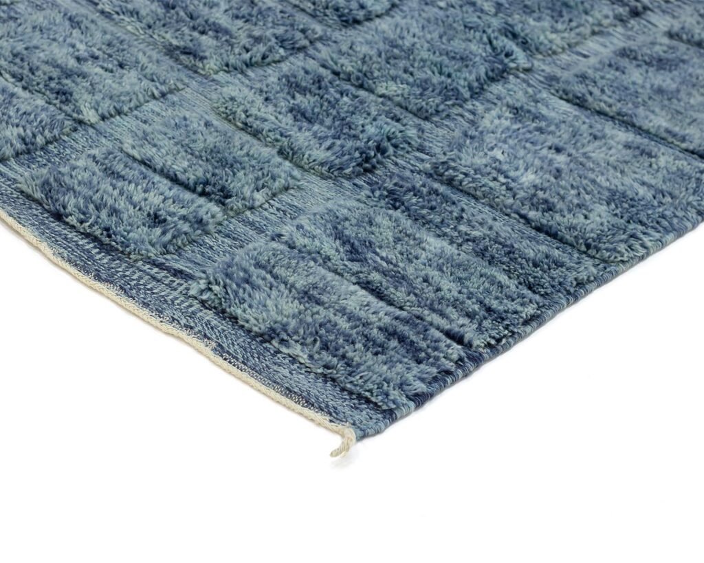 Close-up of a textured blue hand-knotted rug with a grid-like pattern, showcasing a slightly frayed edge reminiscent of Moroccan luxury.