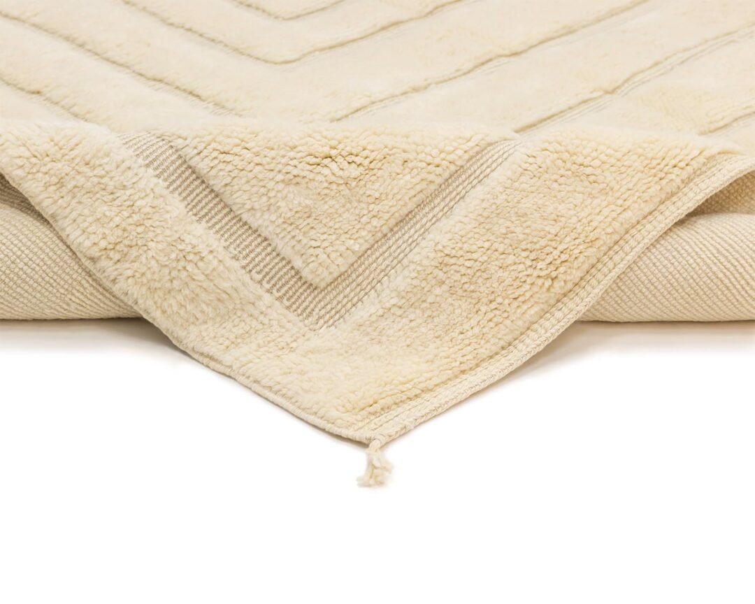 Close-up of a cream-colored textile featuring chevron patterns and a fringed corner, exuding warmth and elegance.