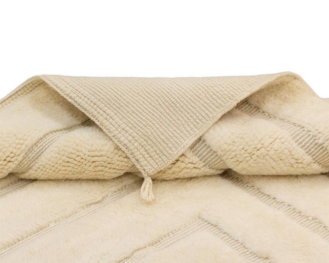 Beige textured fabric folded back, showcasing detailed stitching and a small tassel at the corner. Its soft, inviting appearance adds a touch of elegance to any space.