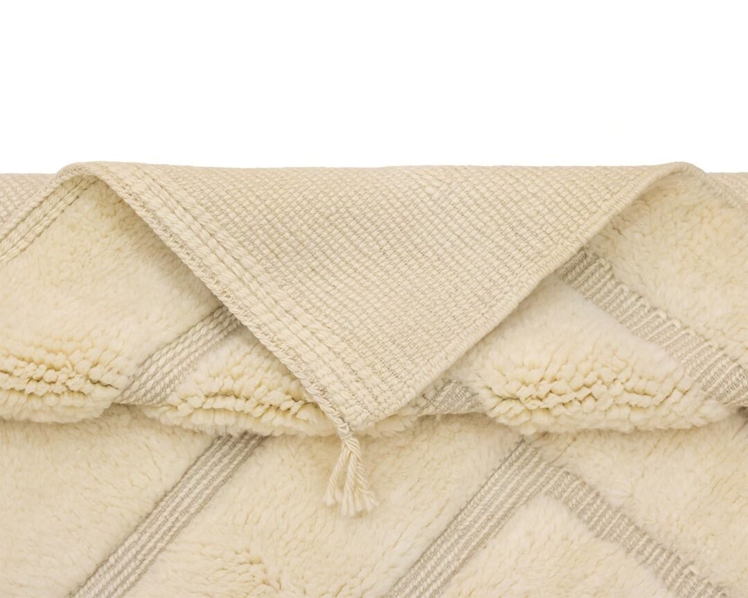 A folded beige textured throw with tassels, featuring a diamond pattern and a soft, fluffy underside.