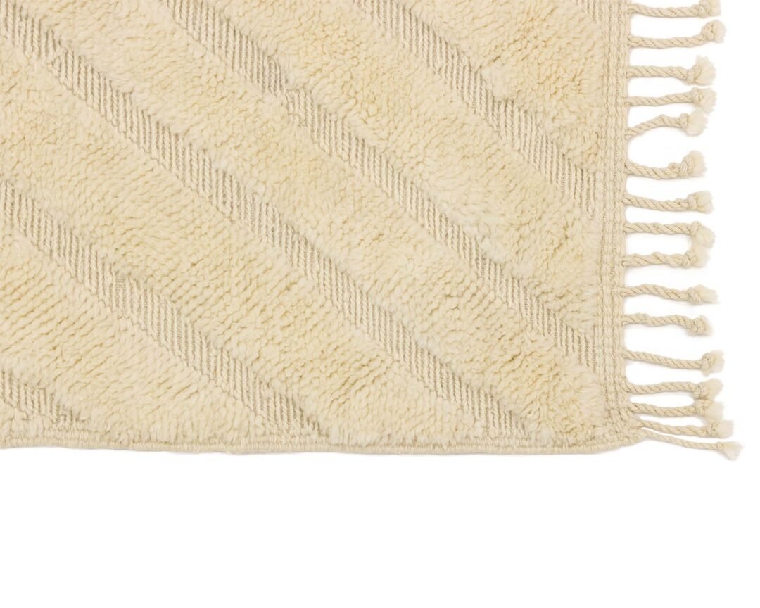 Close-up of a beige textured rug featuring diagonal lines and fringed edges, embodying a modern aesthetic.