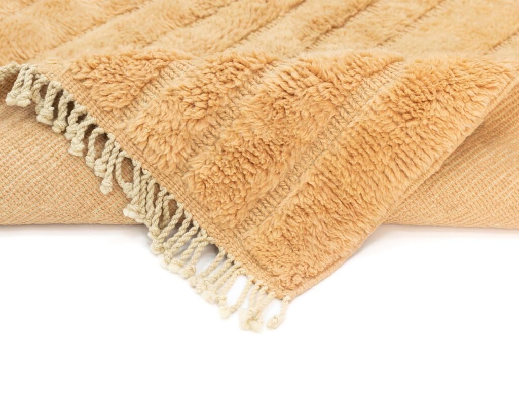 A close-up shot reveals a folded beige fringed throw with a soft, fluffy texture, showcasing woven and textured patterns.