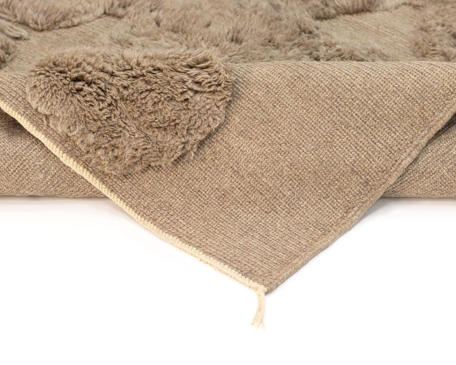 Close-up of a folded beige textured handmade home decor piece with faux fur patches on a white background.