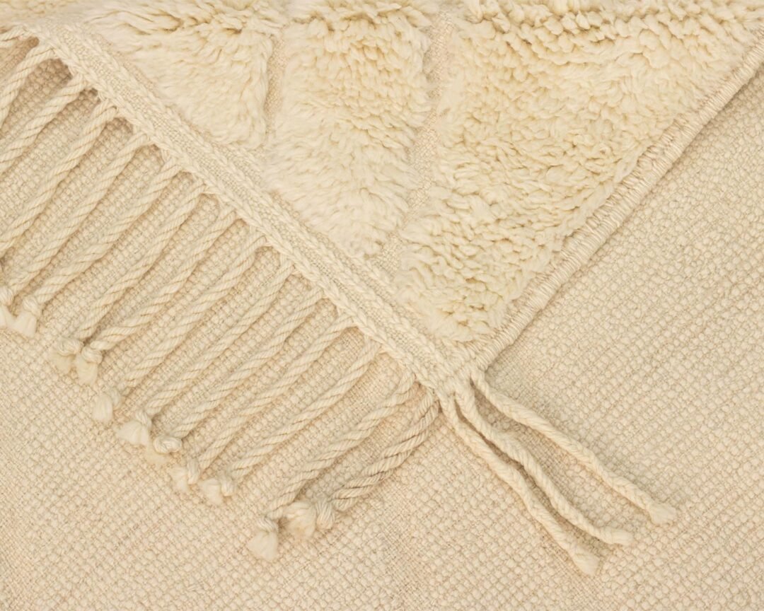 Close-up of a beige woven textile with a textured pattern and fringed edges, showcasing an authentic Moroccan rug.