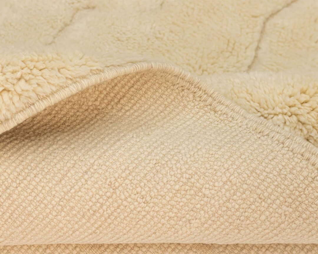 Close-up of a textured, beige fleece piece folded over, revealing the soft, fluffy side and the woven underside reminiscent of an authentic Moroccan rug.