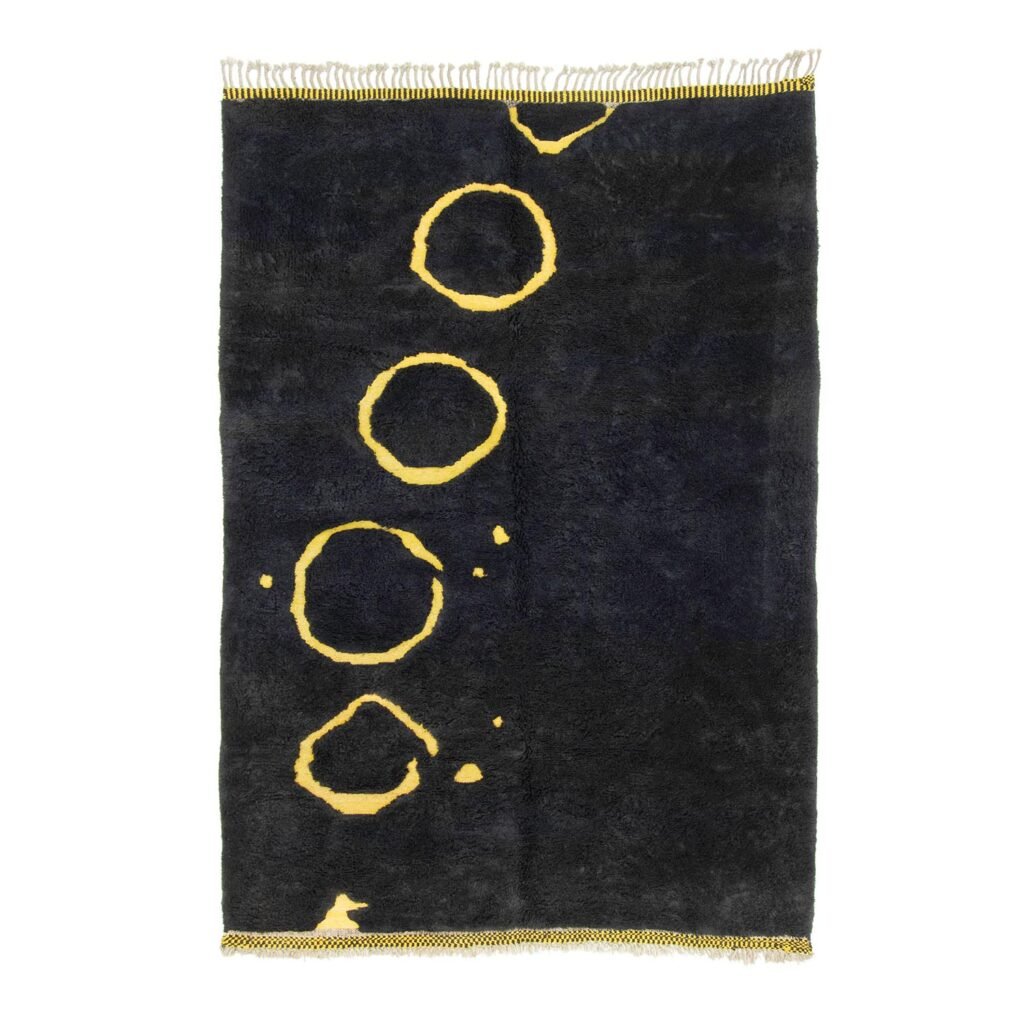 A rectangular dark gray rug with a pattern of scattered, uneven yellow rings on one side. This artisanal rug features hand-knotted craftsmanship and fringes on the shorter edges, echoing the charm of authentic Moroccan rugs.