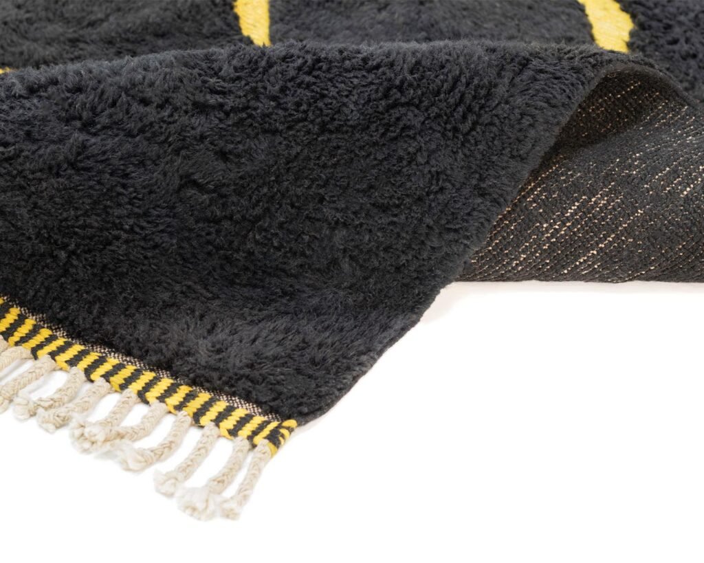A hand-knotted black and yellow fringed rug, partially folded over, reveals its textured surface and intricate weave.