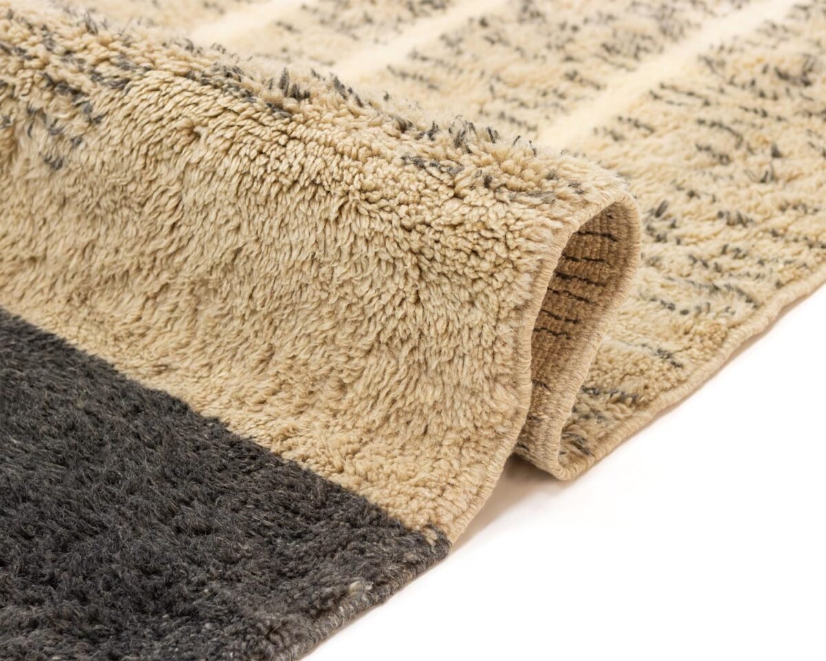 Close-up of a beige and dark gray rug with a visible folded corner, highlighting its thickness and intricate design.