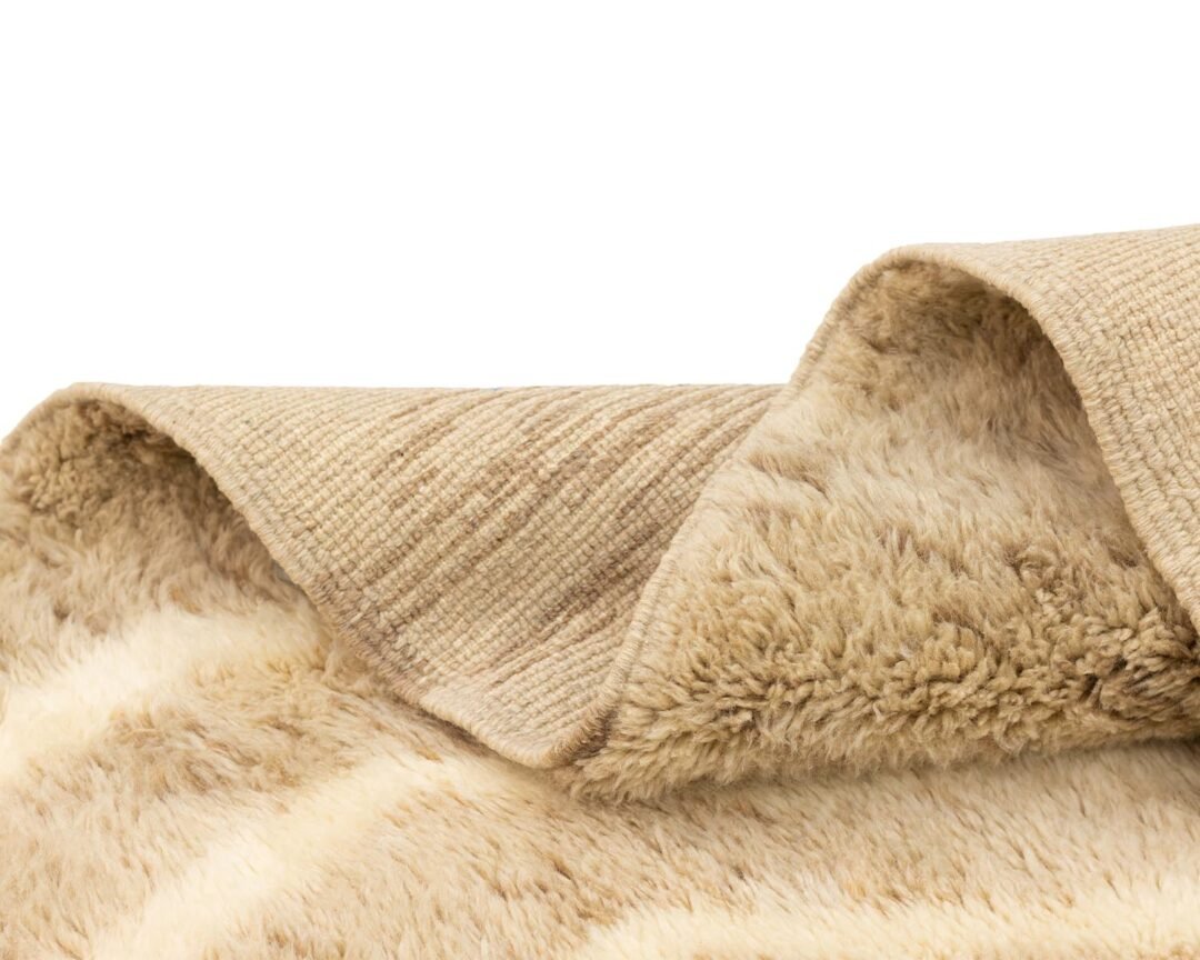 Close-up of a beige and cream faux fur piece with a soft, plush texture. The fabric is draped in folds, revealing its thick, fluffy underside and smooth surface, adding a touch of handmade home decor to any space.