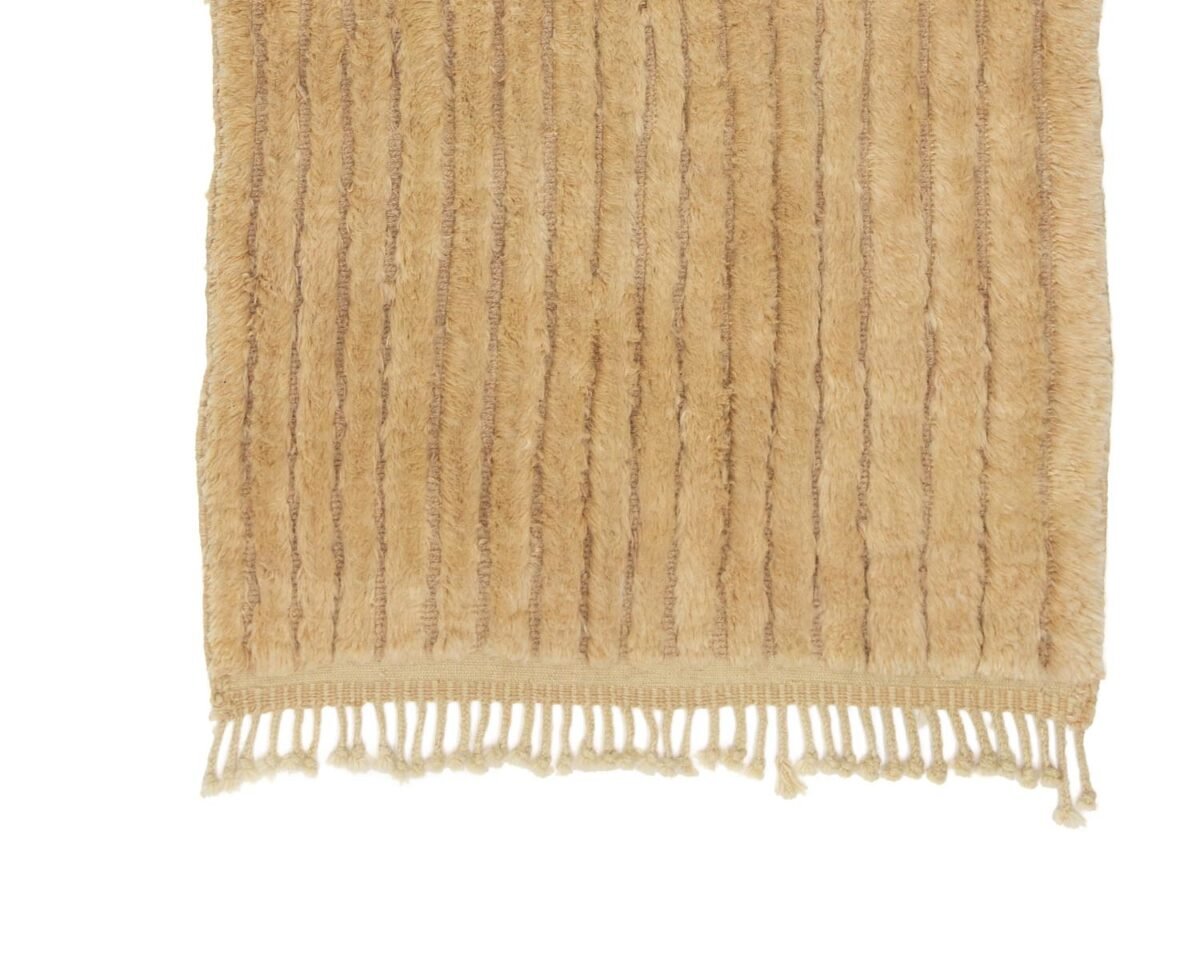 A section of a beige handmade home decor piece features vertical stripes and fringe at the bottom edge.