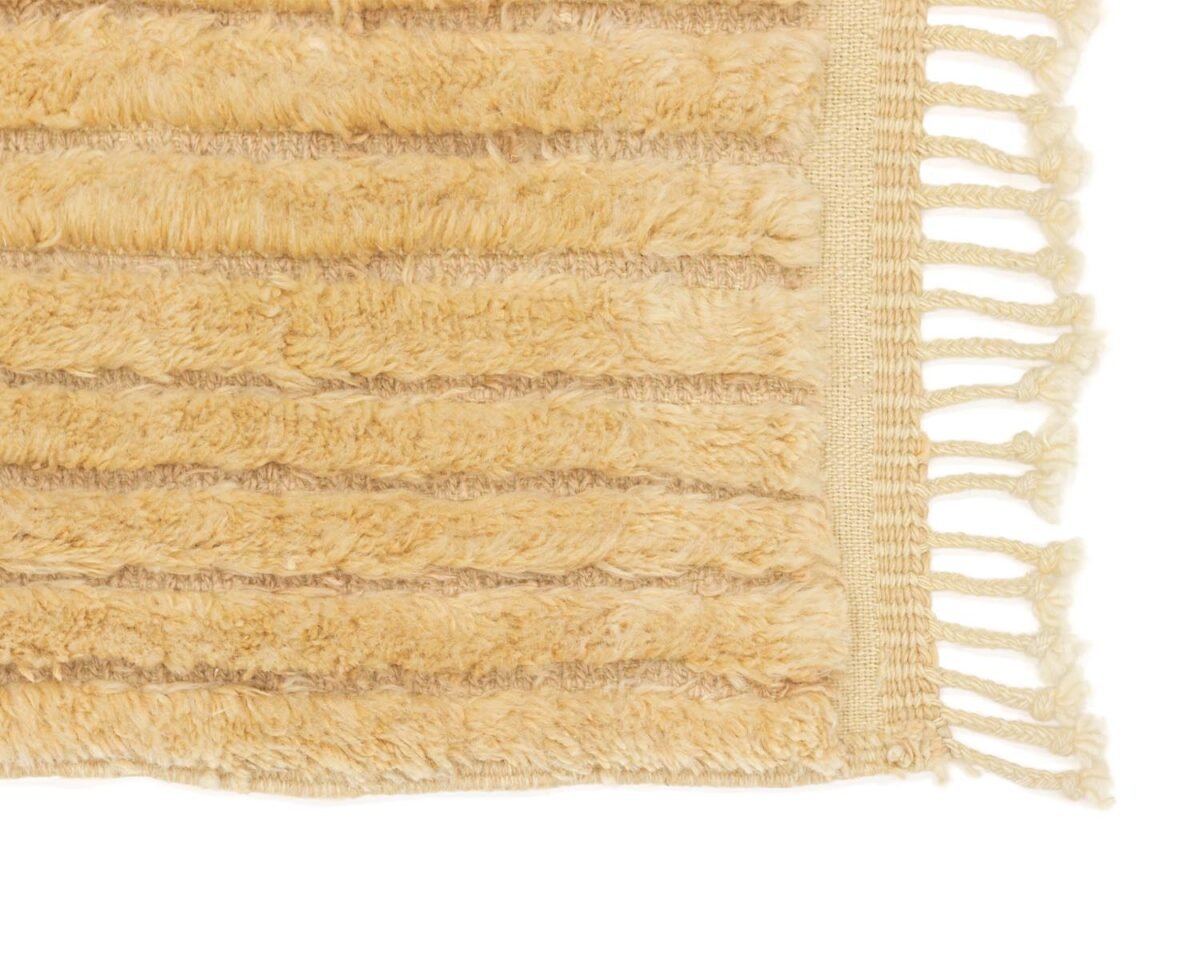 Close-up of a beige, luxurious rug featuring horizontal ridges and elegant fringe along the edge, showcasing the artisan beauty of handmade home decor.