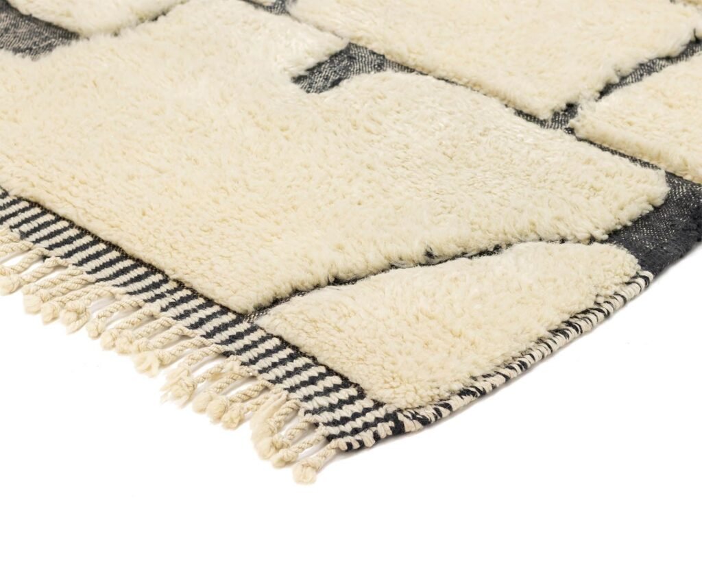 A close-up of a geometric black and white rug showcases its intricate pattern and fringed edges along the bottom side.