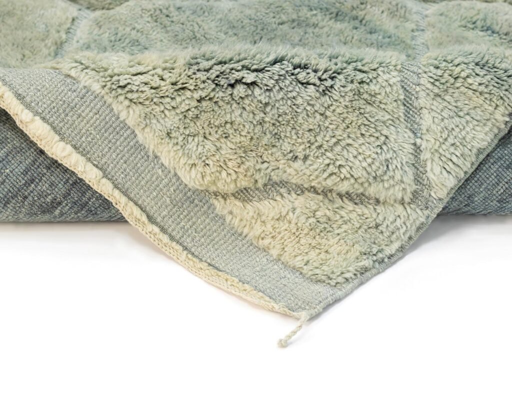 Close-up of a folded light gray shaggy blanket with a textured underside, resting on a white surface.