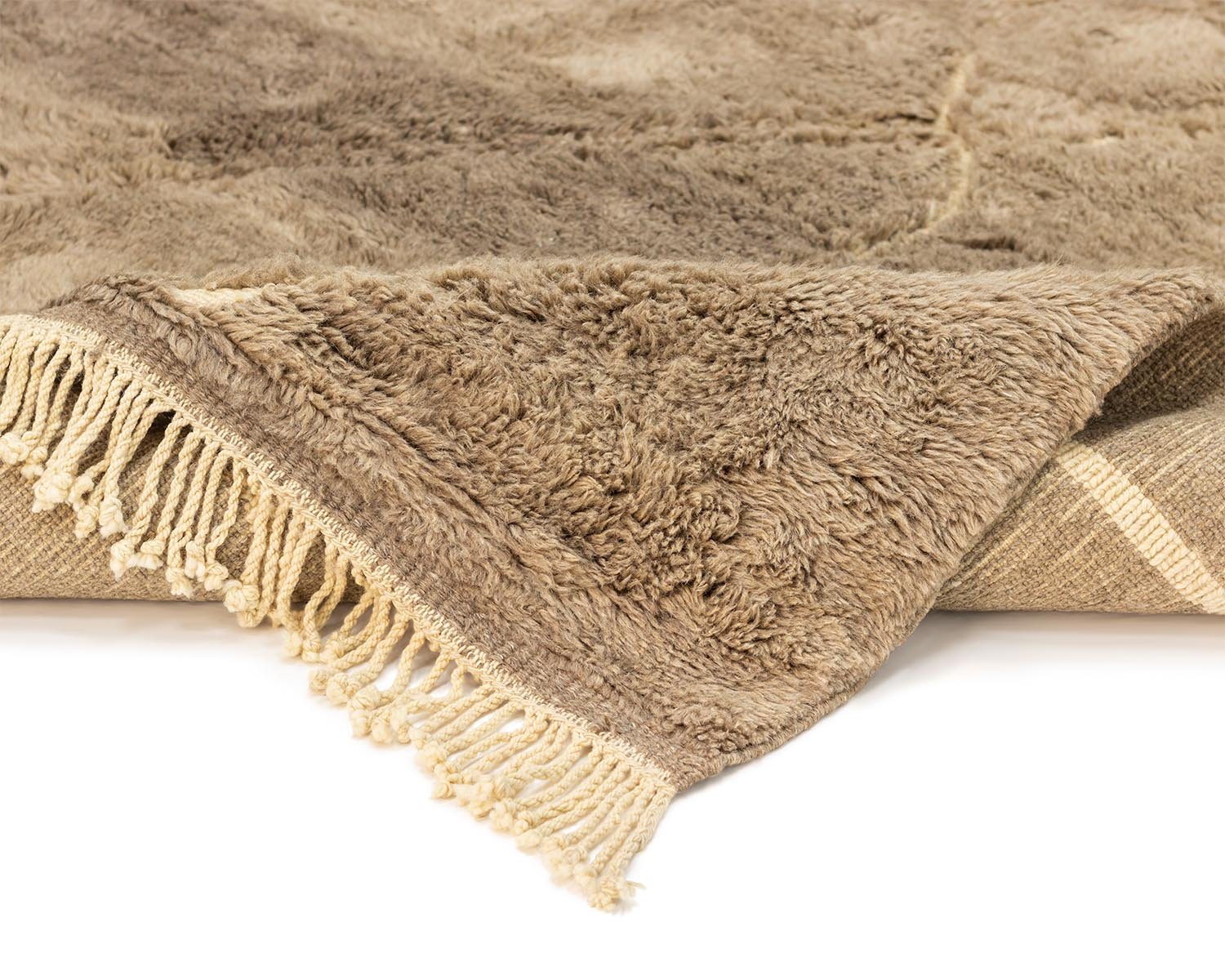 A close-up of a brown fringed rug with a textured, plush surface. The corner is artfully folded over, revealing its underside.