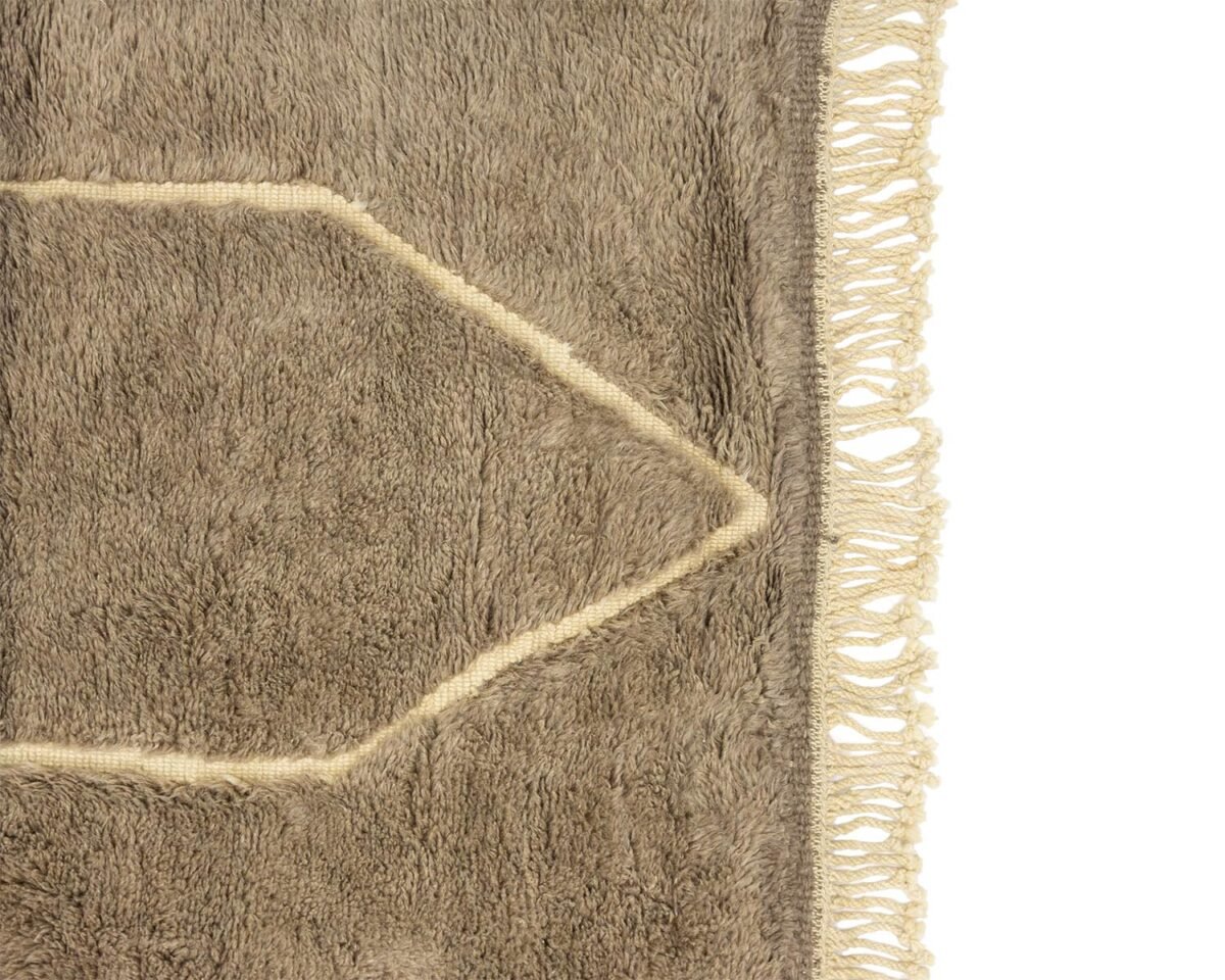 A close-up view of a textured beige rug featuring fringe along the right edge and an intricate geometric pattern at its core.