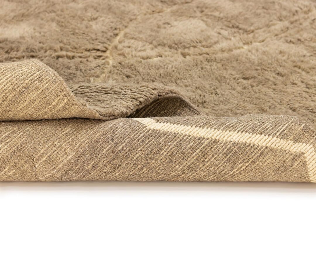 Close-up of a beige, textured area rug with one edge gently folded, revealing its soft pile and woven backing. Perfect for adding warmth to any space, this elegant piece enhances both comfort and style in your room decor.