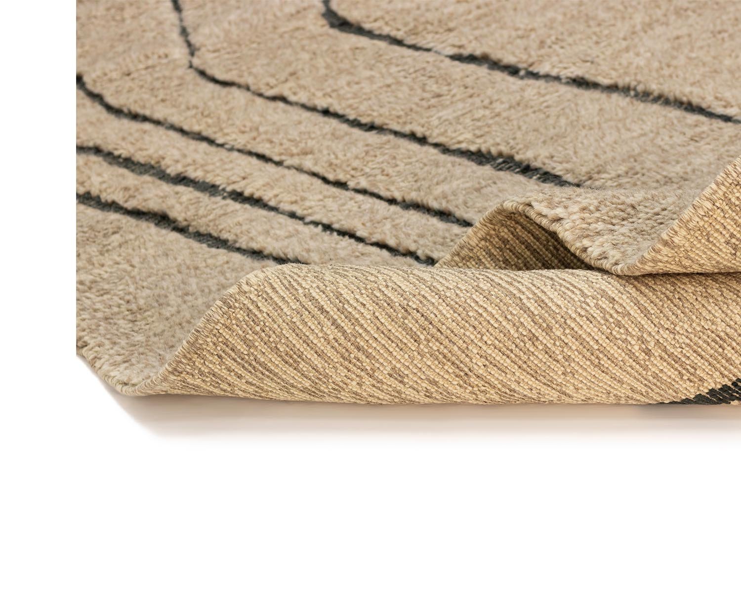 Close-up of a beige artisanal rug corner, highlighting its texture and black linear pattern with the edge slightly folded over.