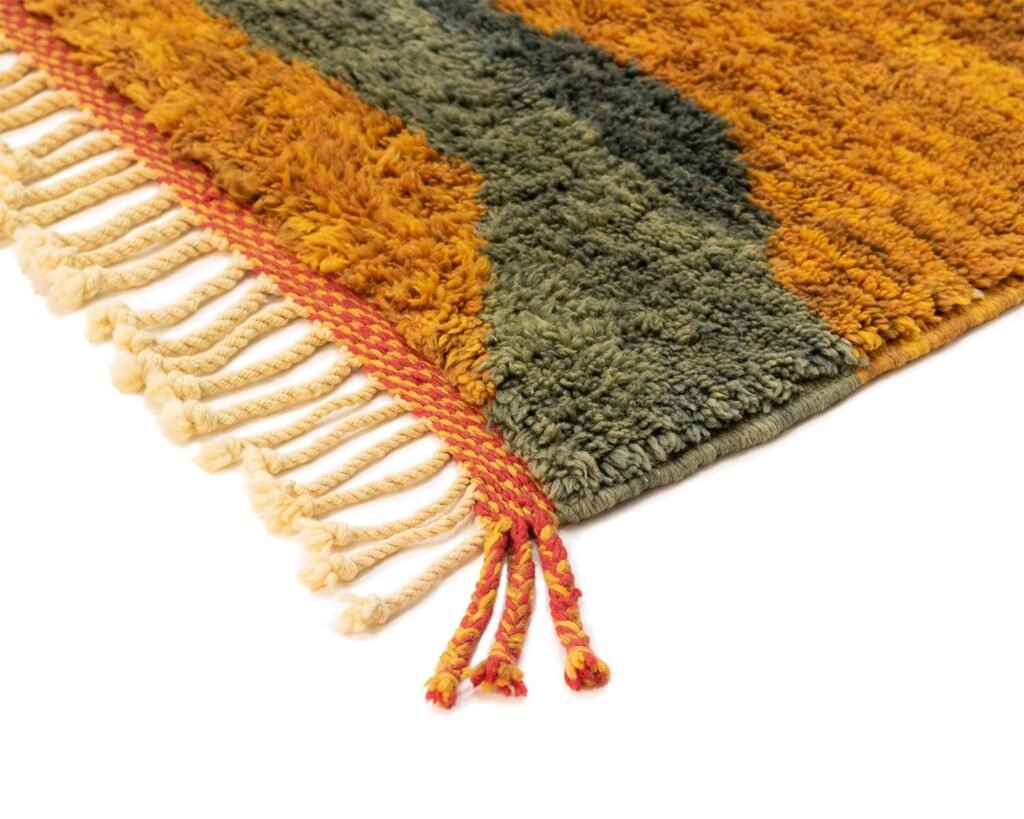 A textured, hand-knotted rug with a fringed edge, featuring a wavy pattern in luxurious shades of orange, green, and yellow.