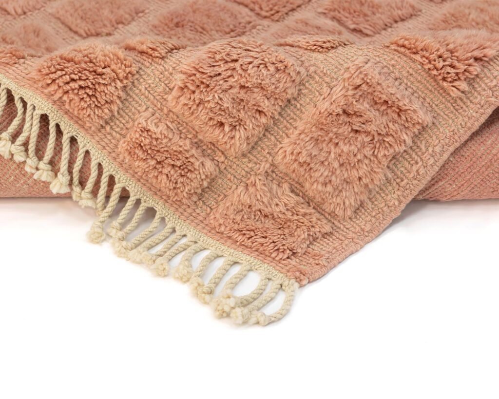 Peach-colored textured Rug with a checkered pattern and fringed edge on a white background.