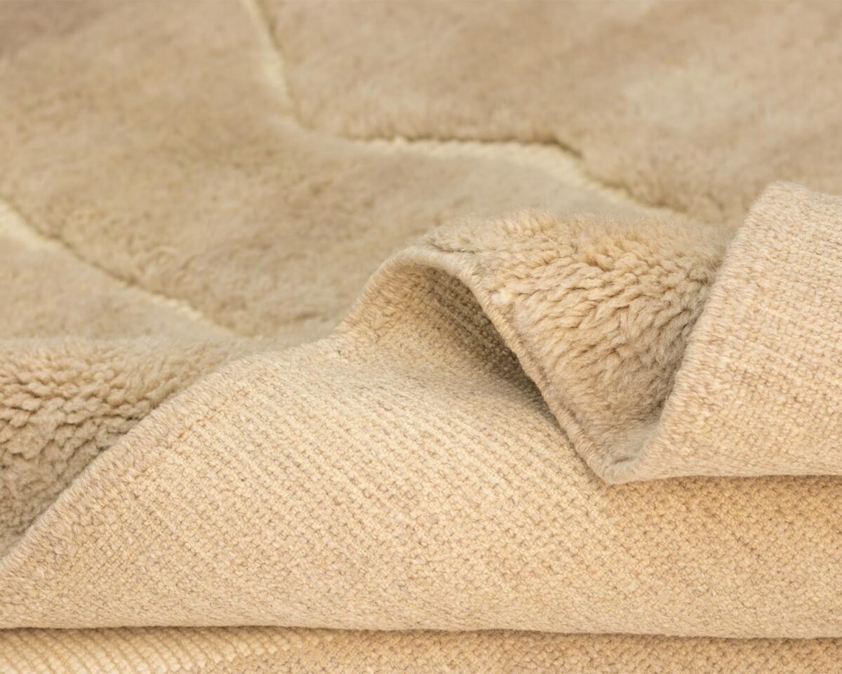 Close-up of a beige, textured masterpiece with a folded corner, revealing a soft, fuzzy surface on top and a woven underside. This piece exemplifies handmade home decor excellence, adding warmth and style to any space.