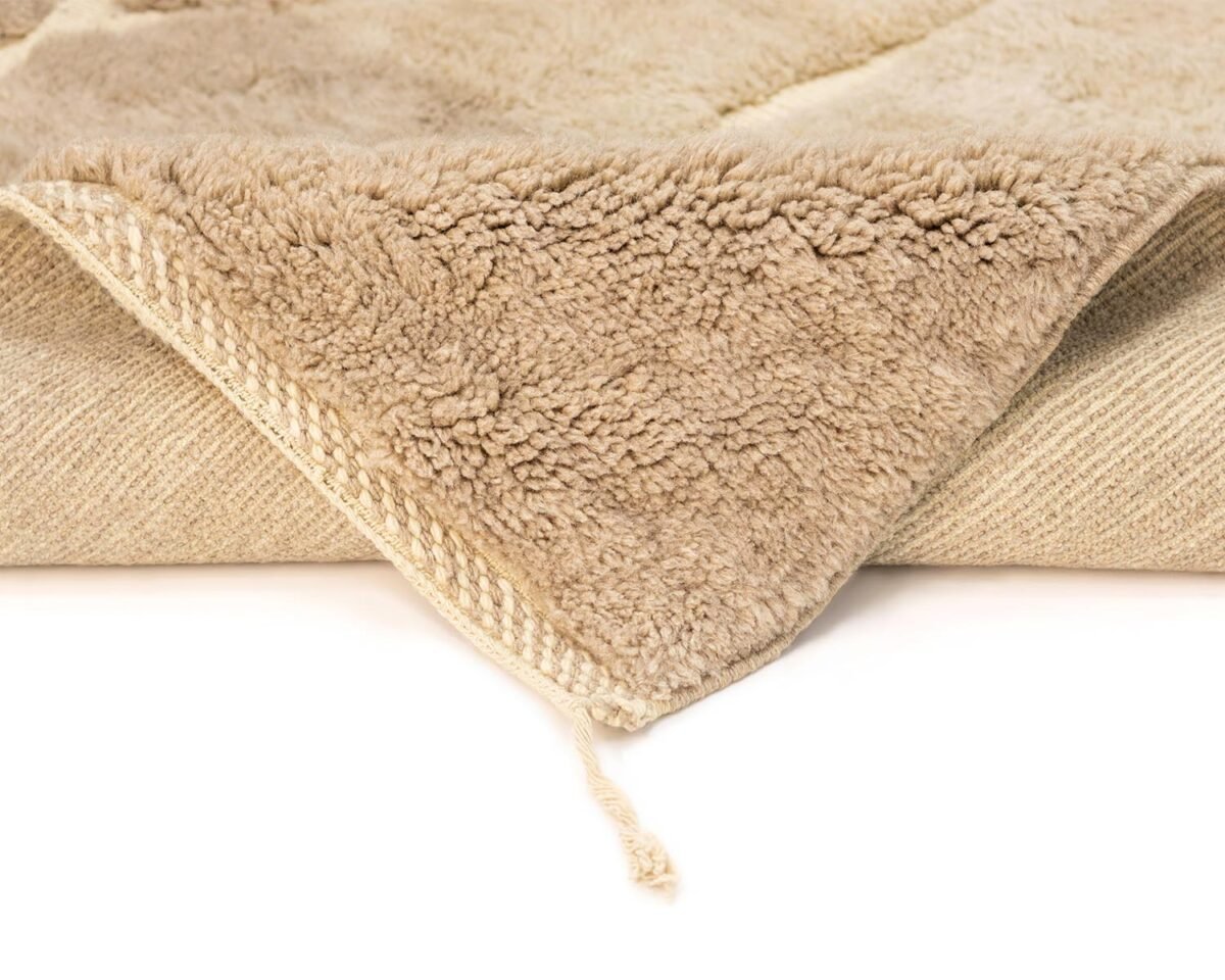 Close-up of a beige, textured fleece piece with a woven edge and a corner folded, revealing both sides. A small string is attached to the corner, adding an element of handmade home decor.