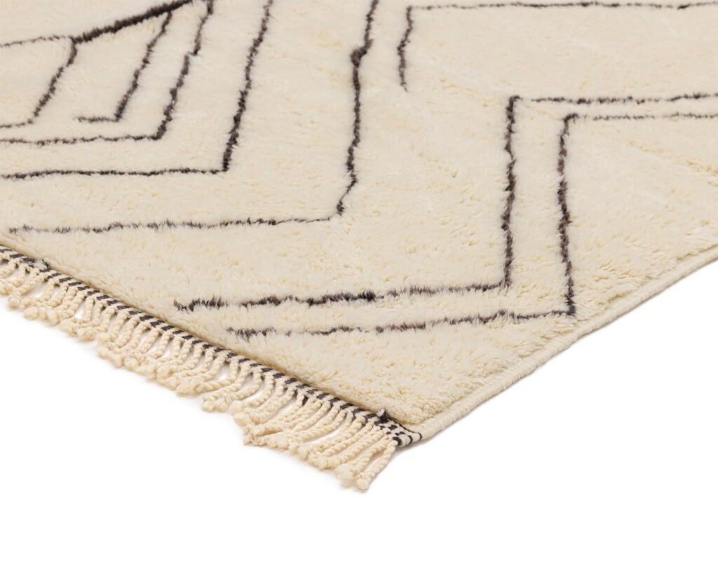 Close-up of a beige rug corner featuring elegant black geometric lines and tassels, ideal for adding style to any room.