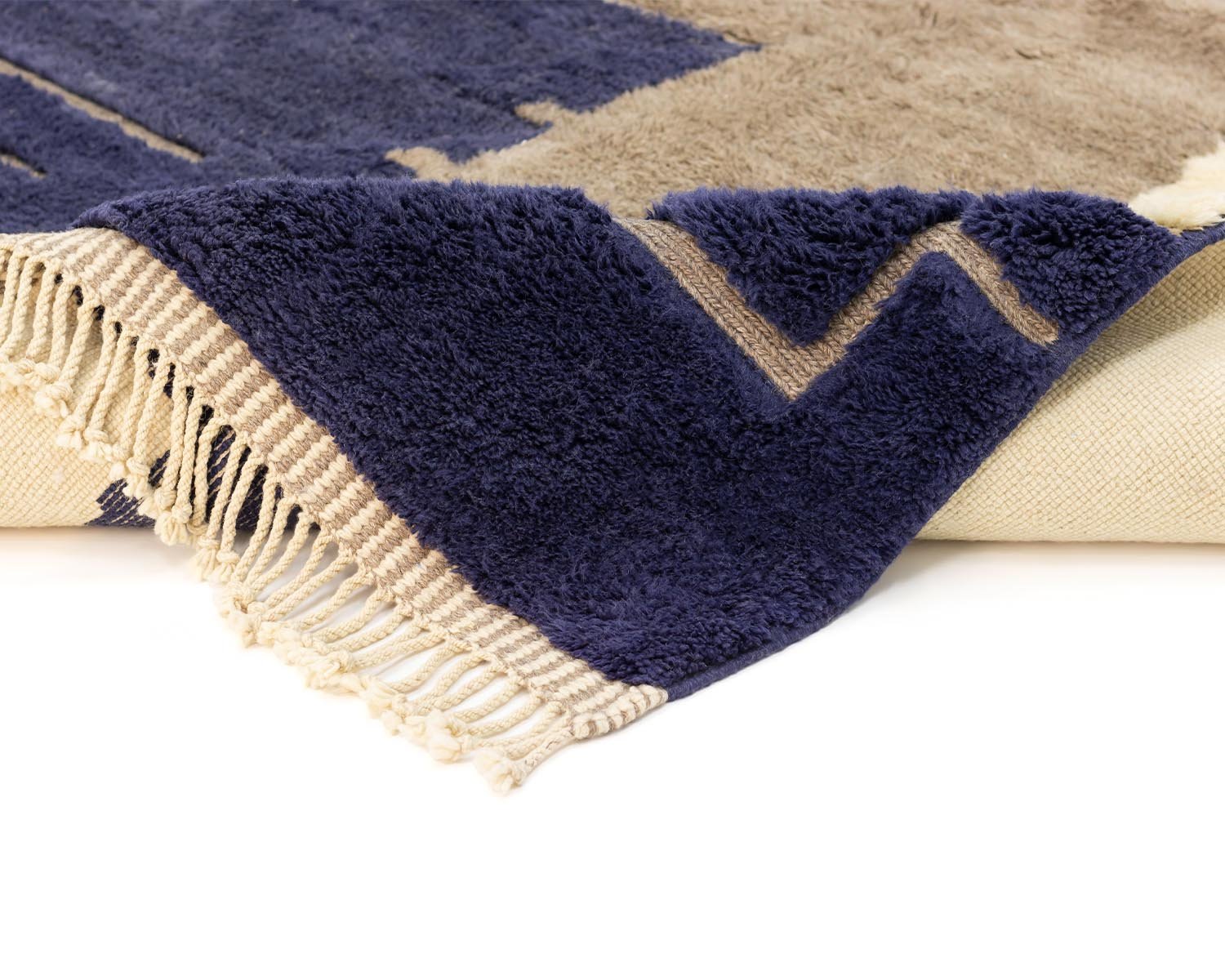 Close-up of a folded rug with fringe, showcasing a striking geometric pattern in navy and beige tones, exuding elegance and charm.