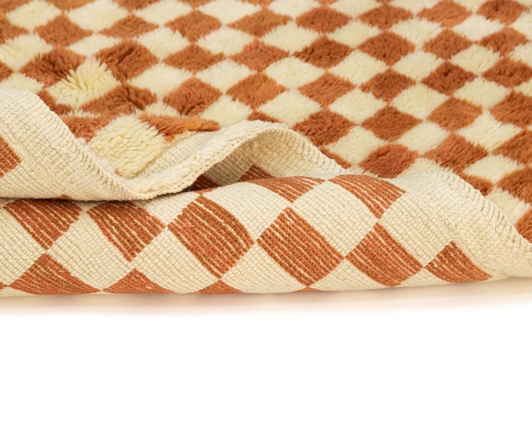 Close-up of a rolled-up textile featuring a checkered pattern in brown and beige tones. The fabric exhibits a soft, plush texture on one side while the other reveals a woven finish, creating an intriguing visual contrast ideal for various interior decor styles.