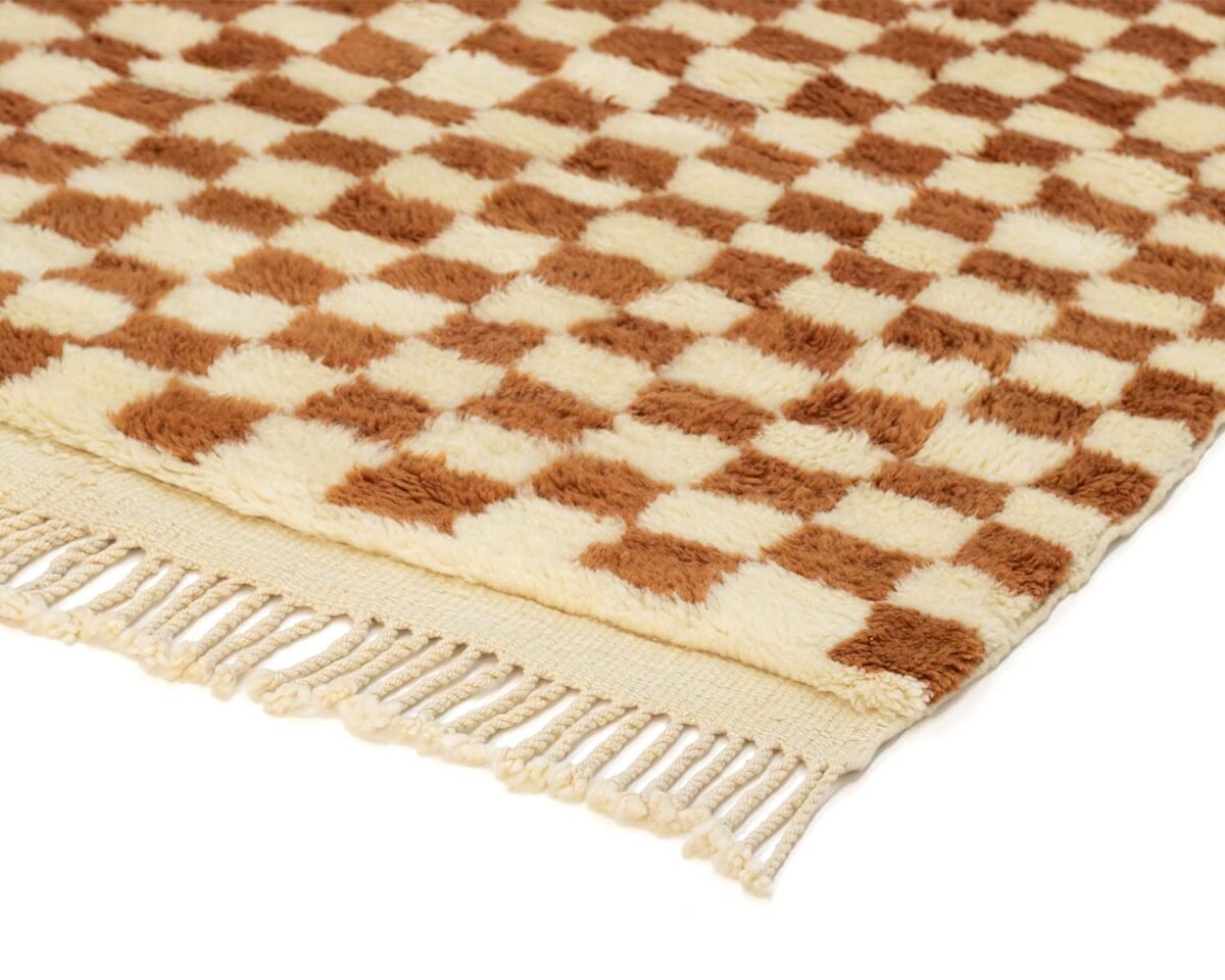 Close-up of a plush rug featuring a brown and beige checkerboard pattern with fringed edges, adding an element of warmth to any space.