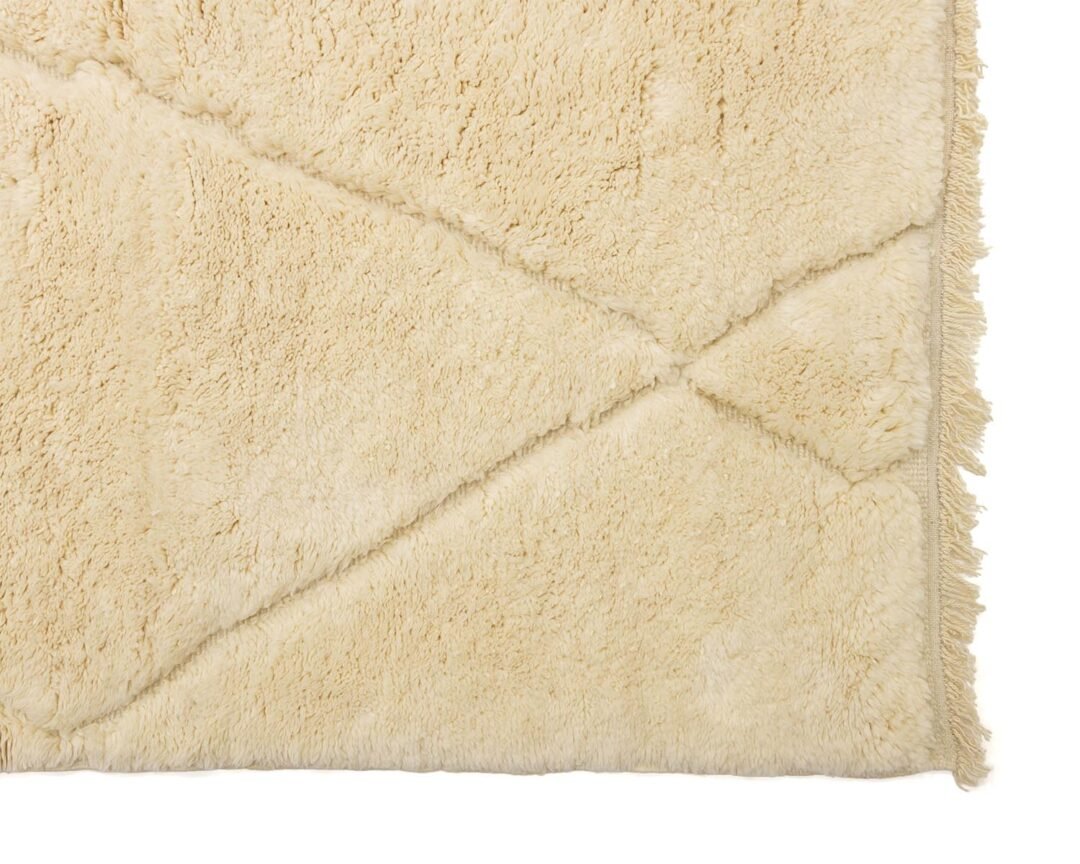 This close-up showcases an artisanal rug with a beige shaggy texture, featuring a diamond pattern and fringed edges.