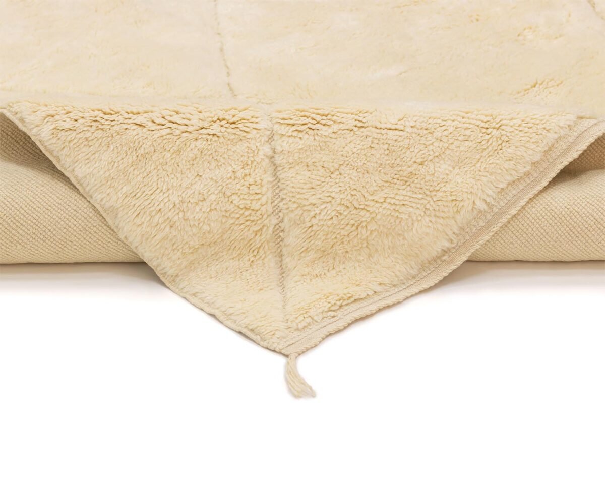 A close-up of an artisanal rug with a folded corner, showcasing its soft, fluffy texture and hand-knotted edges.