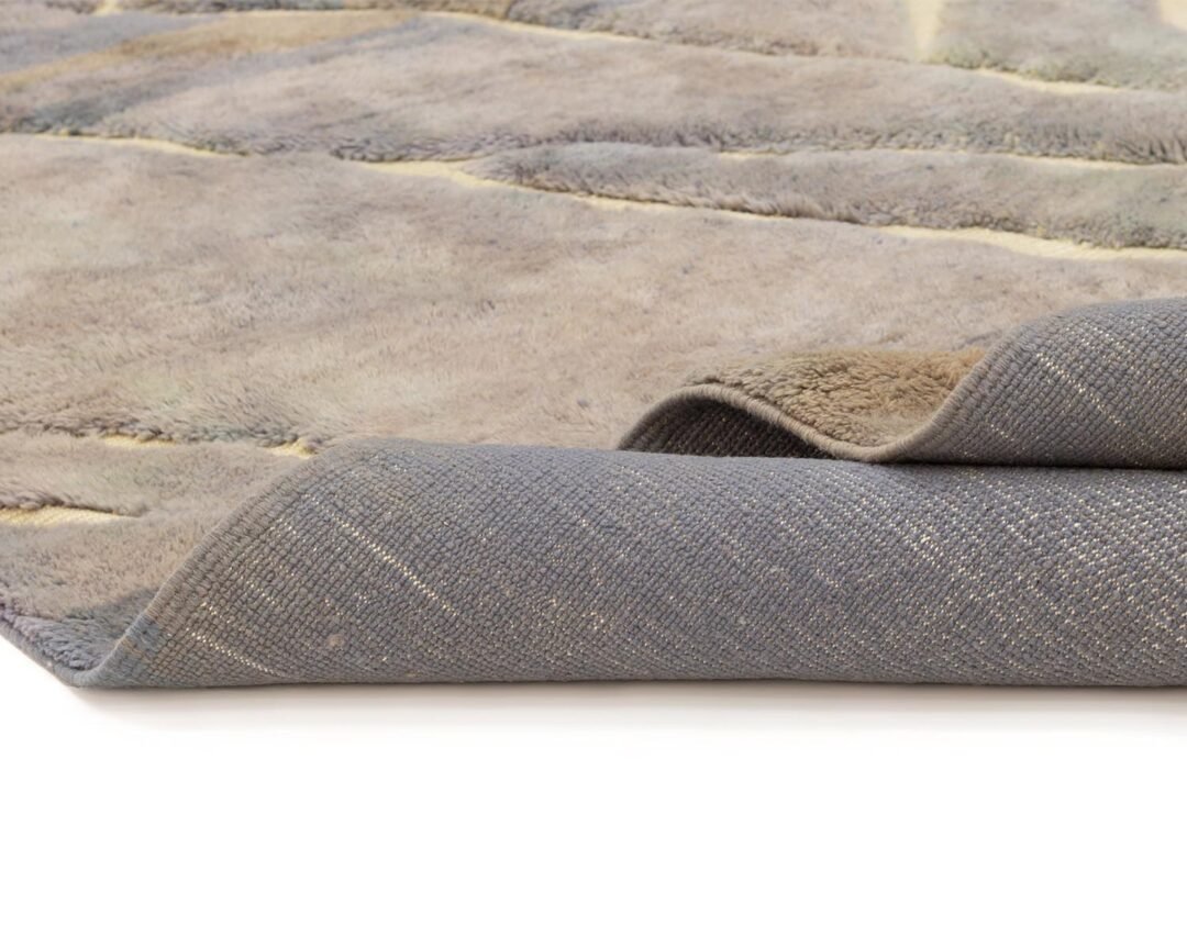 Close-up of a folded luxury rug with a soft, fuzzy texture on top and a woven fabric underside, displayed on a white surface.