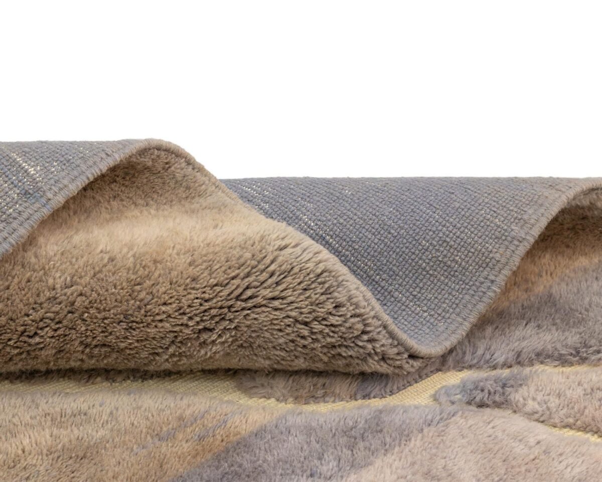 Close-up of a luxury rug, featuring a thick, fluffy gray and tan texture on one side and a woven gray backing on the other. This exquisite piece embodies the essence of handmade home decor.