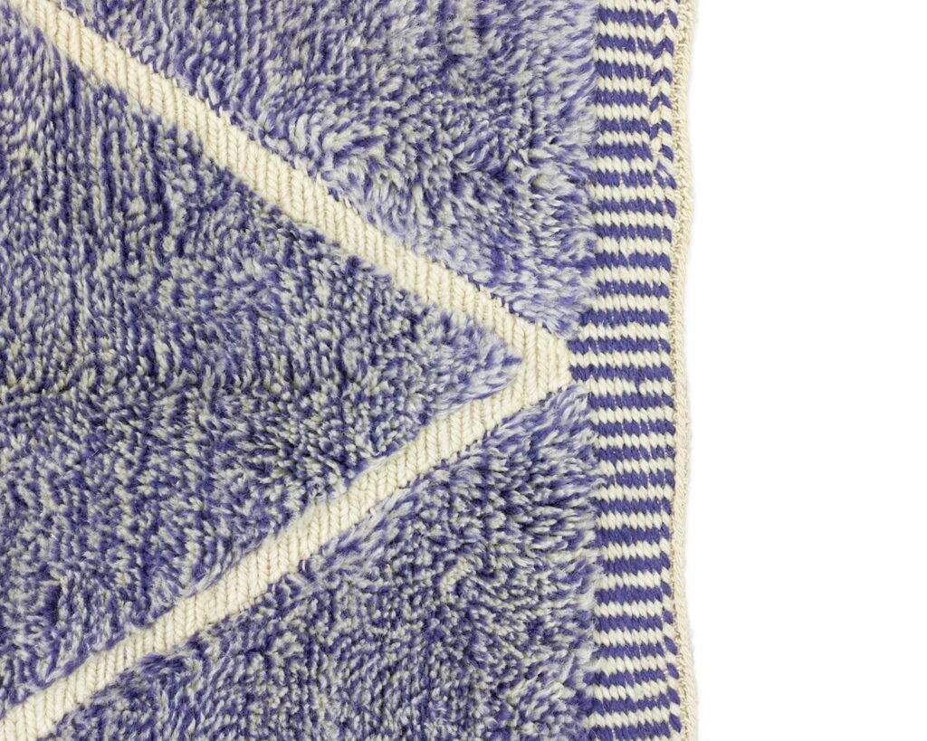 Close-up of a textured purple and white chevron-patterned fabric, reminiscent of an authentic Moroccan rug, with a striped border on the right.