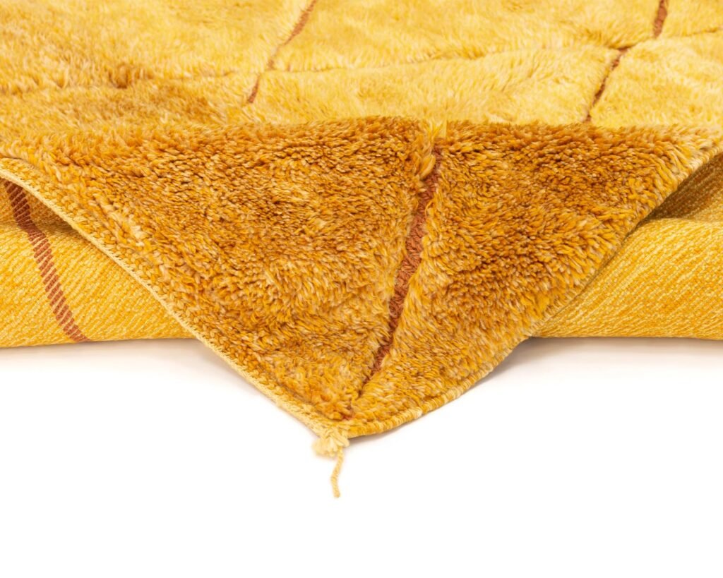 A close-up of a textured yellow and brown rug showing its soft fabric and fold at the corner.