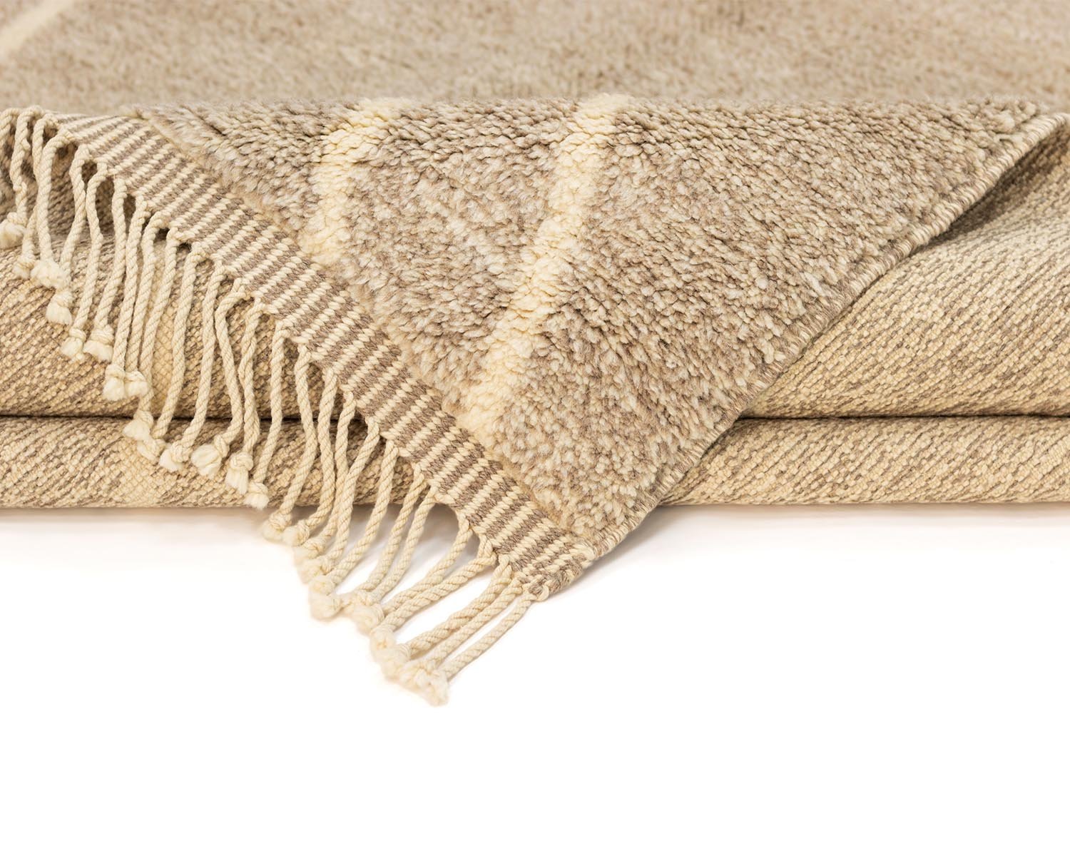 A folded beige woven throw with fringe detailing on one edge, featuring subtle diagonal stripes for a touch of elegance.