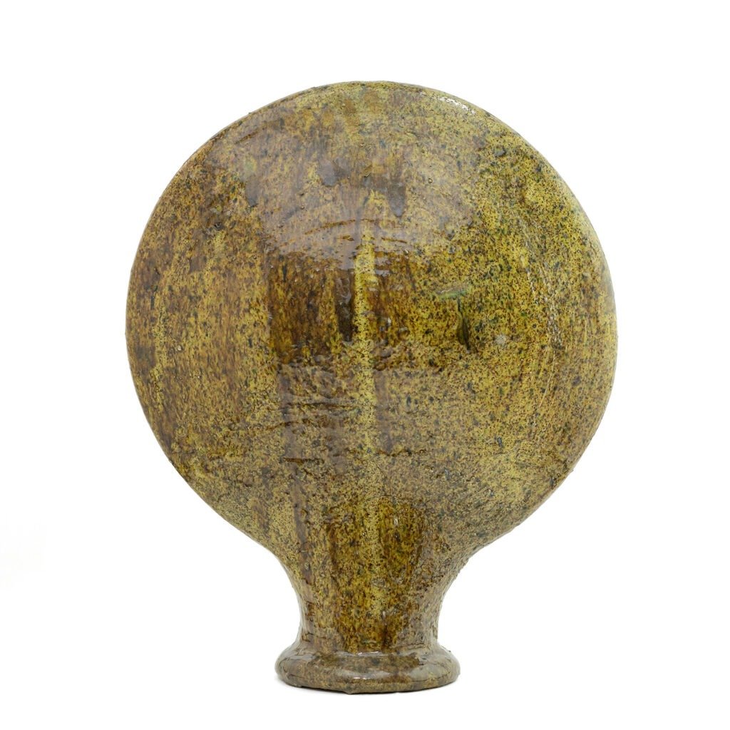 A round, greenish-brown ceramic object with a smooth surface, spherical body, and a small cylindrical base, standing upright against a white background.