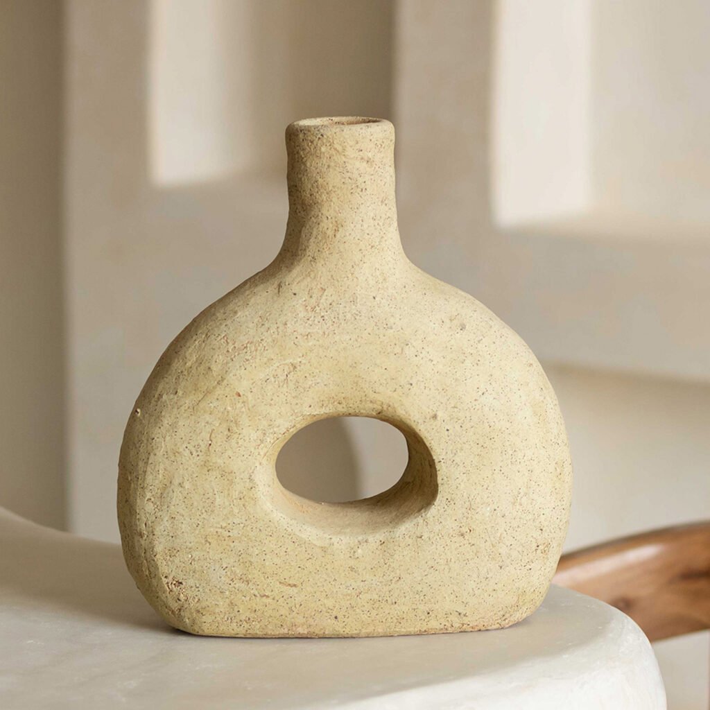 Beige, unglazed Tamegroute pottery vase with a textured finish, hollow center, and rounded top, elegantly placed on a smooth, light-colored surface.
