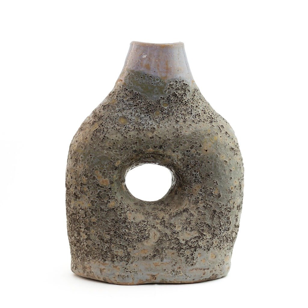 A textured, stone-like ceramic sculpture reminiscent of Glazed Tamegroute pottery features an open circular hole in the center, tapering to a narrow top.