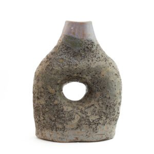 A textured, stone-like ceramic sculpture reminiscent of Glazed Tamegroute pottery features an open circular hole in the center, tapering to a narrow top.