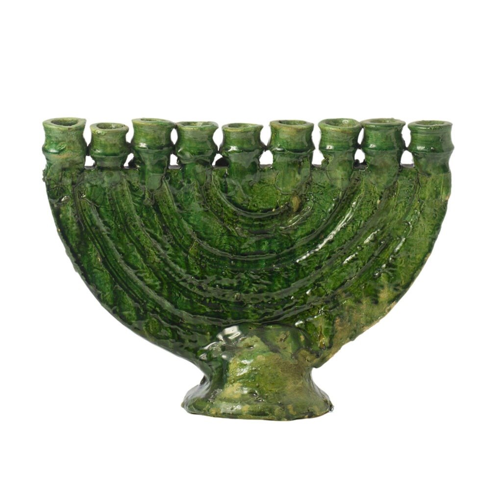 A green ceramic menorah crafted in the style of Tamegroute pottery, showcasing nine candle holders arranged in a row and adorned with a textured, wave-like pattern on its surface.